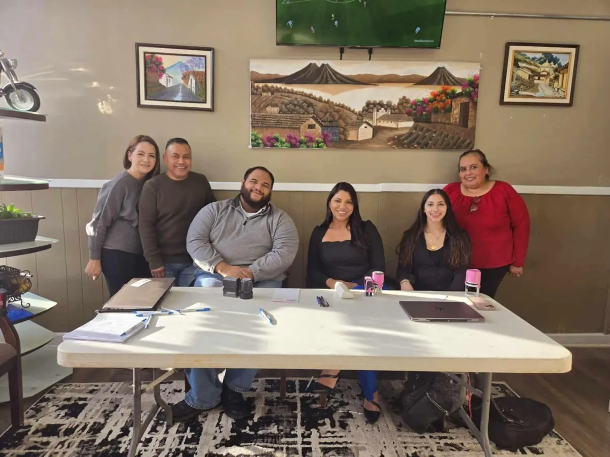 Equipo de Raíces Center sonriendo detrás de una mesa de atención a la comunidad