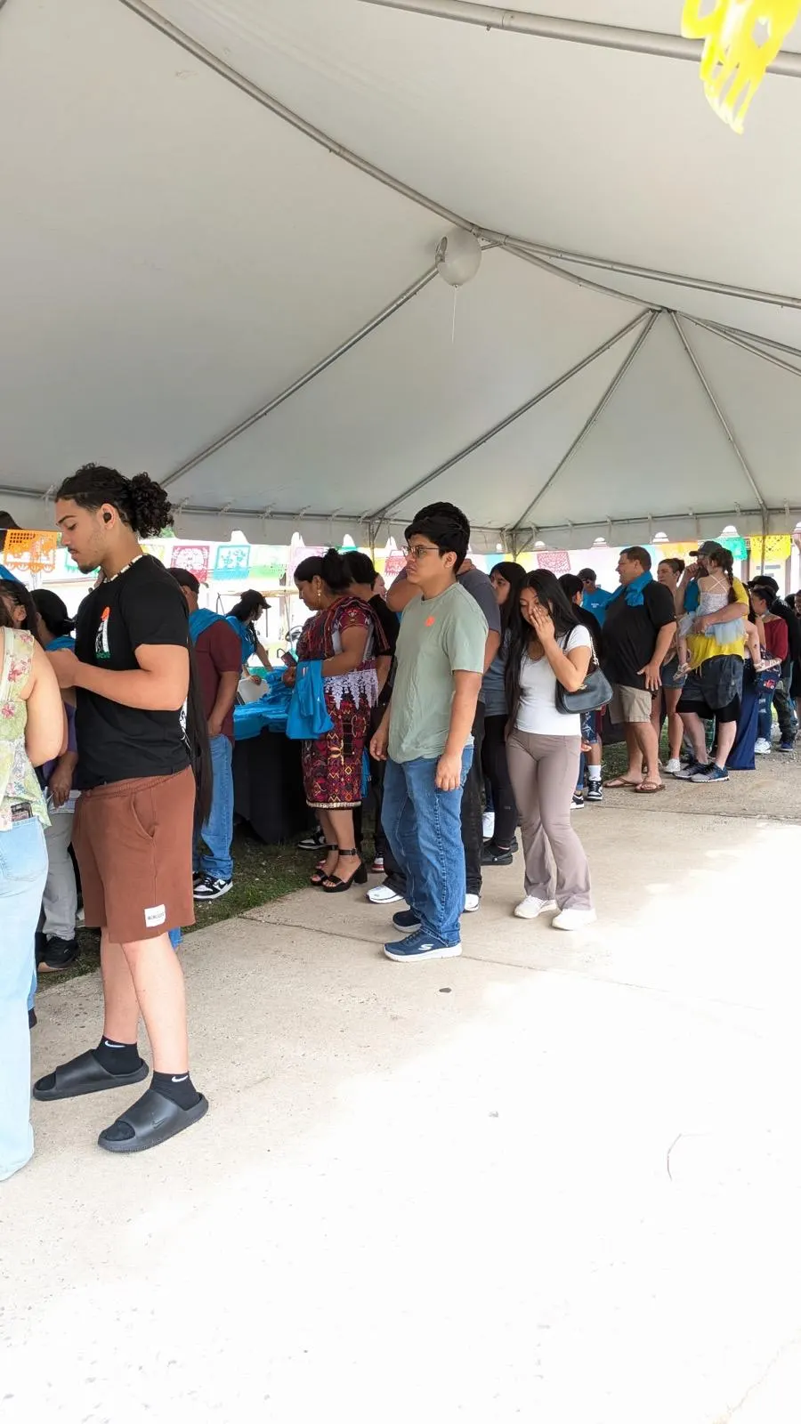 Familias hacen fila bajo una carpa decorada con papel picado durante un evento comunitario